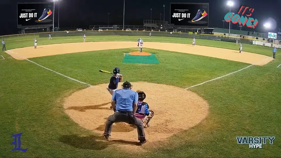 A baseball field at night with ads displayed on the two outfield screens