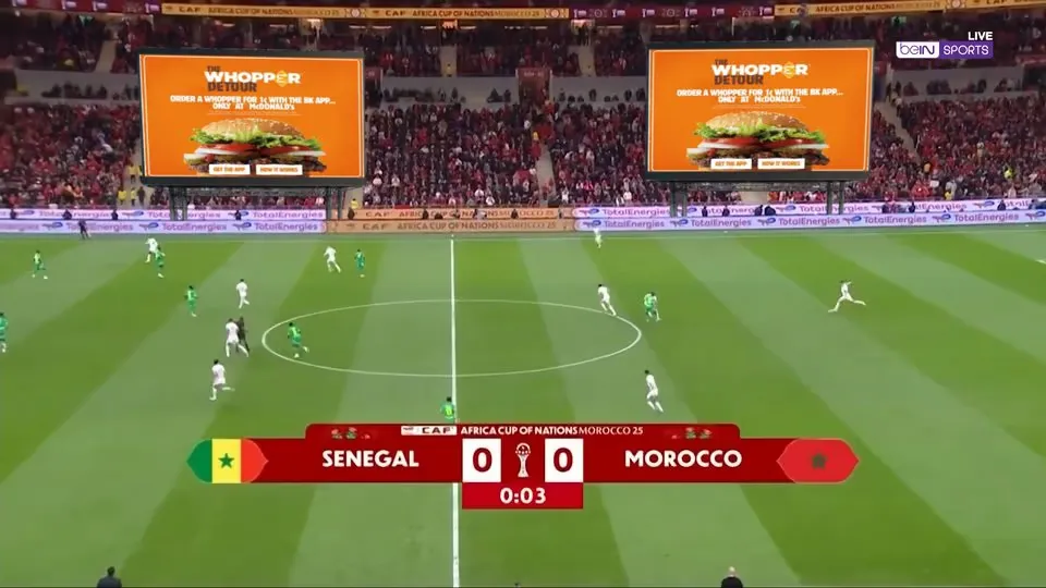 A football stadium with ads displayed on two large screens above the stands